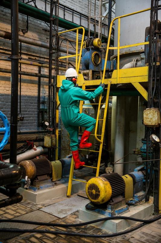 man in safety gear climbs ladder inside industrial facility
