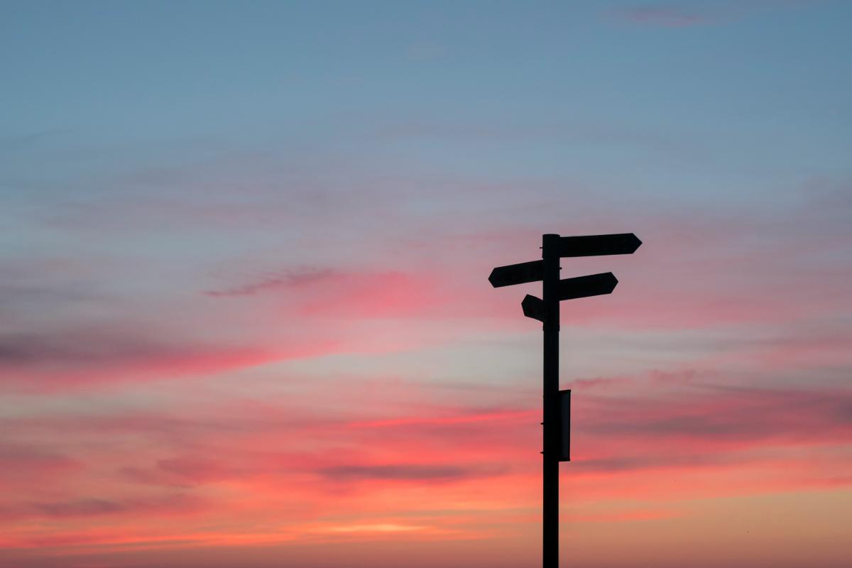 A dark street sign at dusk with orange and blue skies in the background